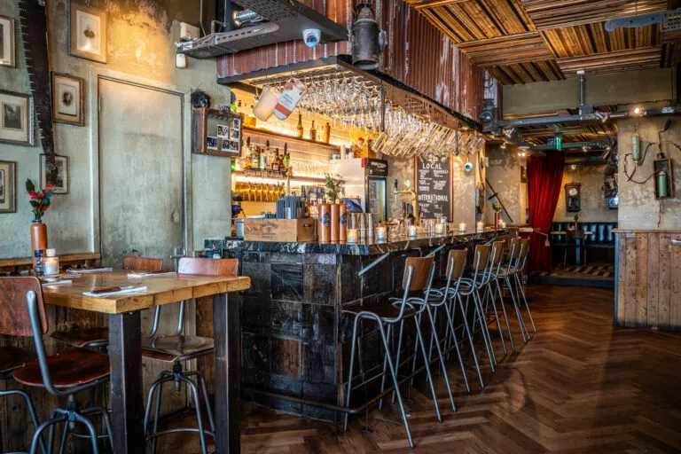 Long bar with high stools and herringbone floor at Cannibale Royale Handboogstraat
