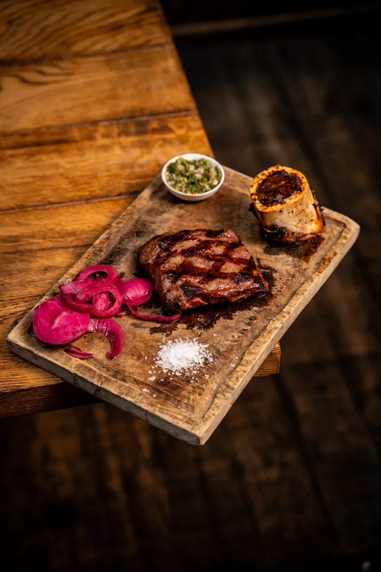 Le Modeste, flat iron steak with grill marks on a wooden board with chimichurri, red onion and sea salt